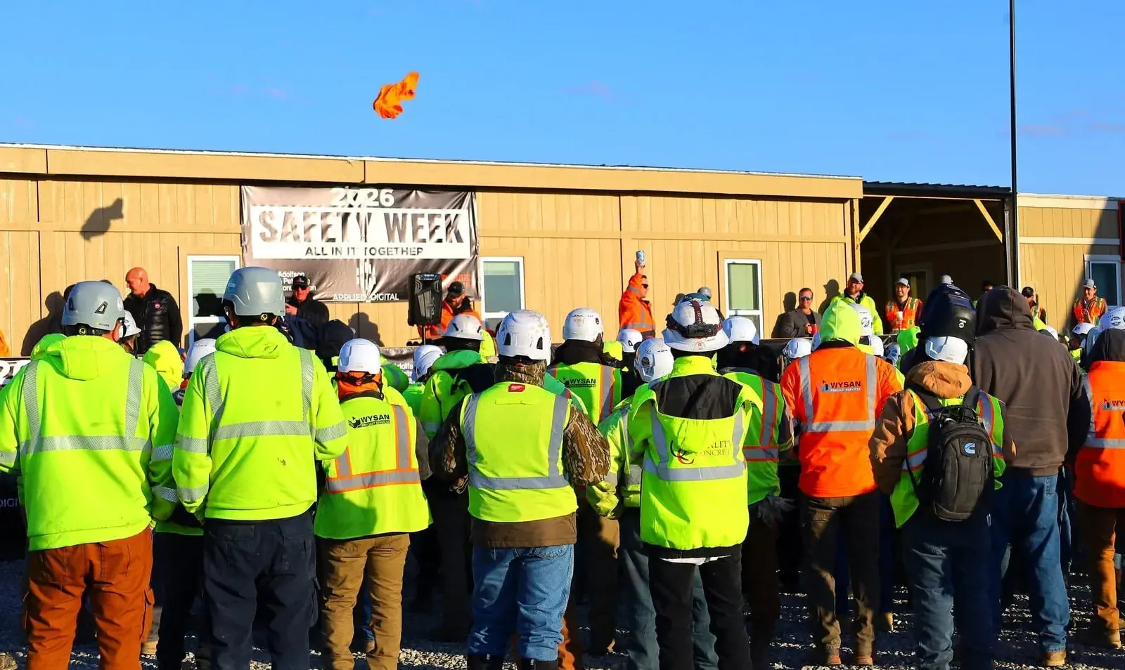 Workers in high-visibility gear gathered in front of the 2026 Safety Week 'All In It Together' banner during the Harwood jobsite safety event